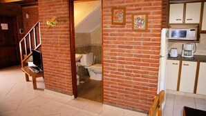 A room with a brick wall, a wooden staircase, a toilet, a microwave, and a coffee maker. - Cabañas Madre Tierra (Valeria del Mar)