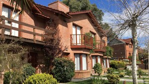 A brick building with multiple balconies and windows, surrounded by greenery and a paved area. - Cabañas Madre Tierra (Valeria del Mar)