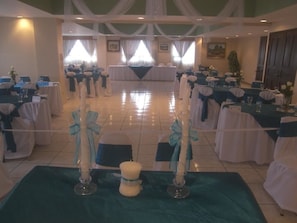 Formal banquet hall with rows of tables set for a seated event, featuring white tablecloths and blue sashes.
