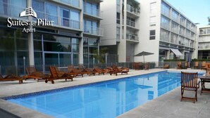 Una piscina con lettini e ombrelloni, circondata da un edificio moderno con balconi.