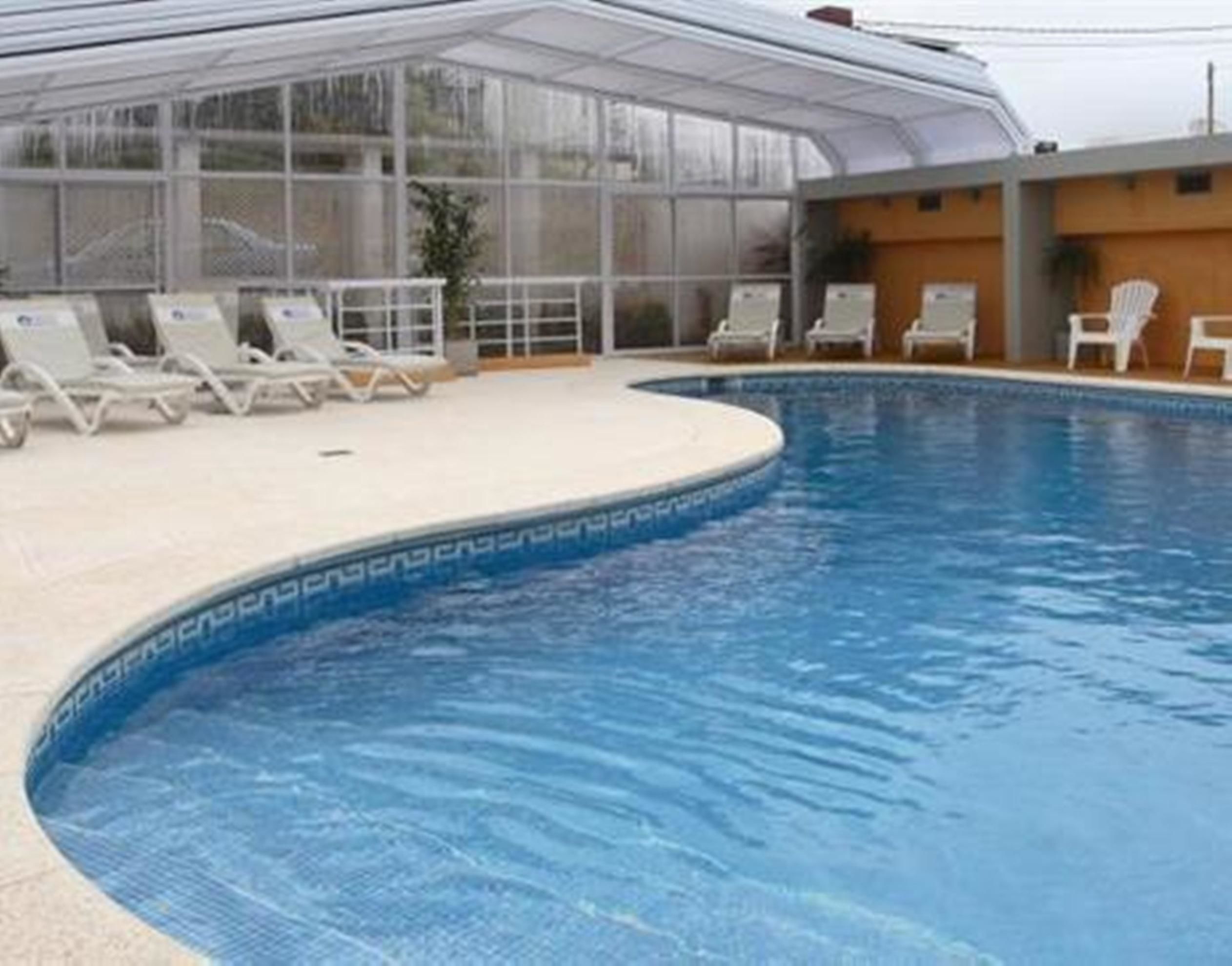 A swimming pool with a glass enclosure, lounge chairs, and a tiled deck.