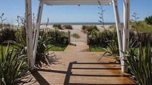 A wooden pathway leading to a beach with a white pergola structure. - Parada 47 Apart de Playa (Villa Gesell)