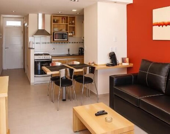 A compact living space with a kitchenette, dining area, and a seating area with a couch and coffee table. - Parada 47 Apart de Playa (Villa Gesell)