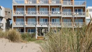 A multi-story hotel with balconies, located near a beach with tall grass in the foreground. - Parada 47 Apart de Playa (Villa Gesell)