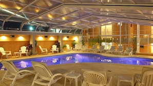 An indoor swimming pool with white lounge chairs and a glass ceiling. - Parada 47 Apart de Playa (Villa Gesell)