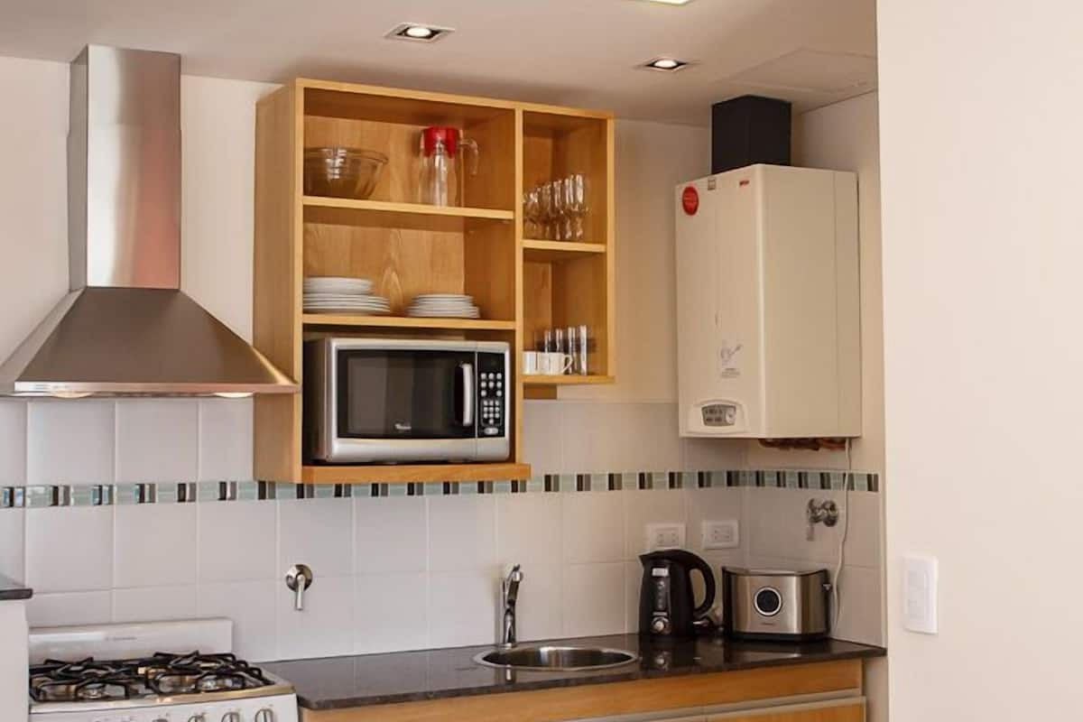 A compact kitchen with a stove, microwave, and cabinets. There is a dining table with chairs.