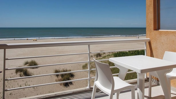A balcony with a white table and chairs, overlooking a sandy beach and the ocean. - Parada 47 Apart de Playa (Villa Gesell)