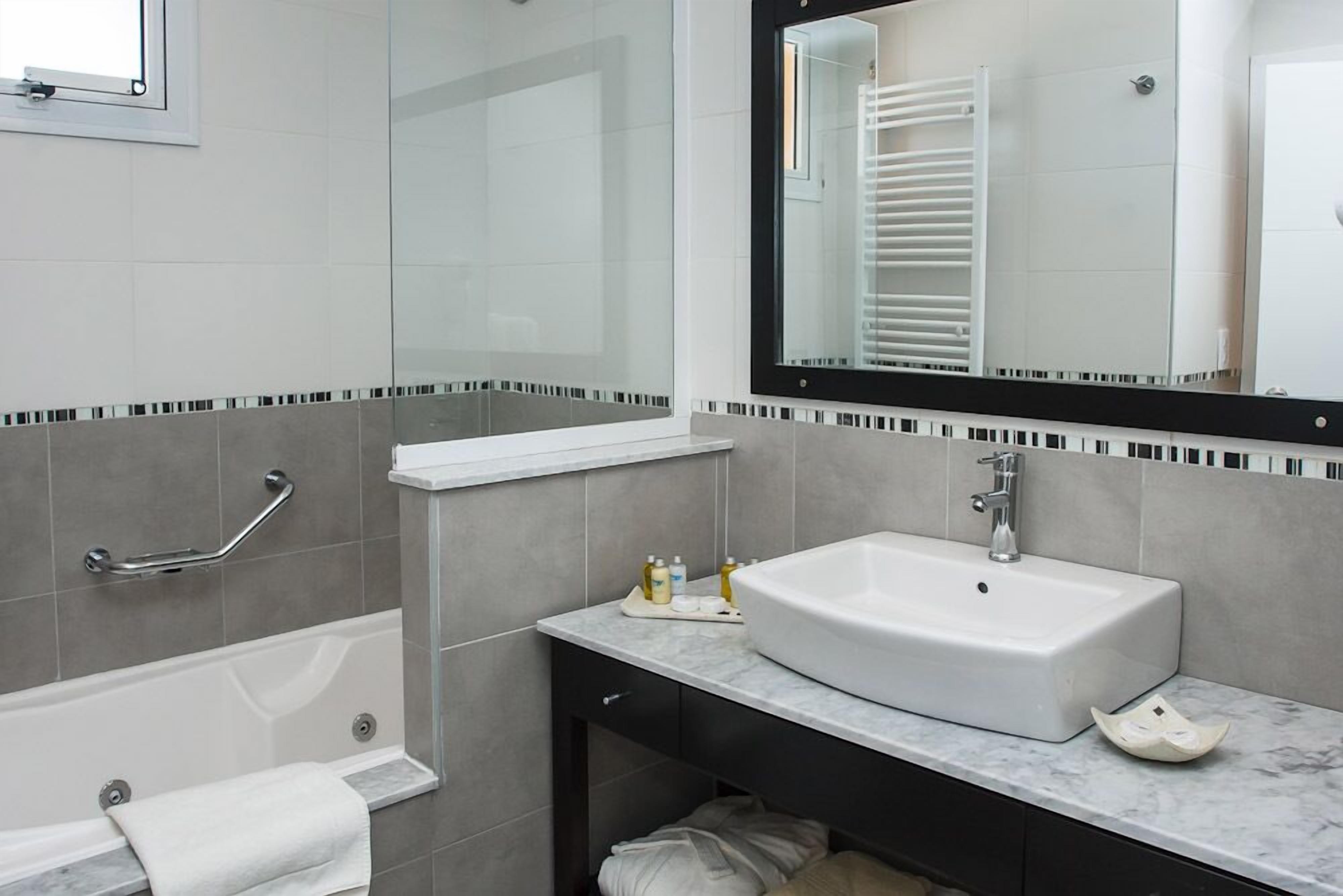 Un baño moderno con un lavamanos blanco, una cabina de ducha con paredes de vidrio, un perchero para toallas y un espejo.