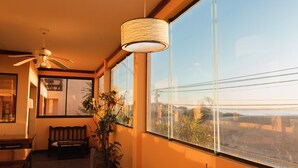 A room with a large window, a ceiling fan, a bench, and a potted plant. - Complejo Playa Norte (Mar de Ajo)