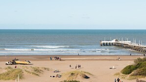 A beach with a pier extending into the ocean, sandy beach, and people walking and relaxing. - Complejo Playa Norte (Mar de Ajo)