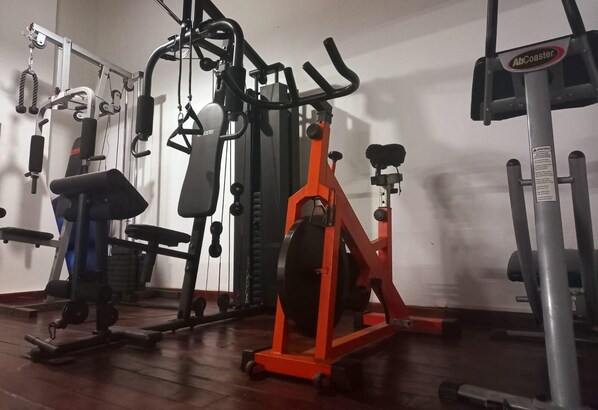 A gym with various exercise machines, including a red elliptical, a black weight machine, and a blue bench. - Complejo Playa Norte (Mar de Ajo)
