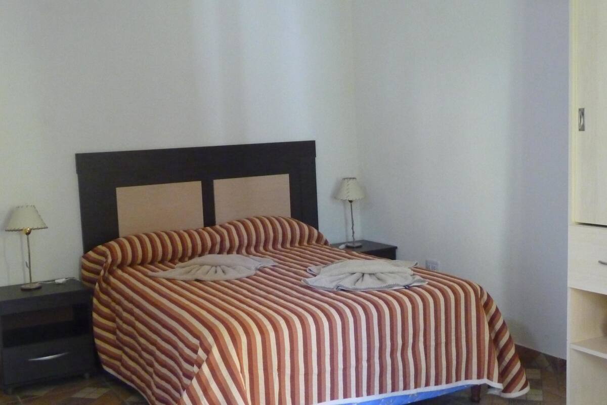 A hotel room with a bed, two bedside tables, a lamp on each table, and a wardrobe.