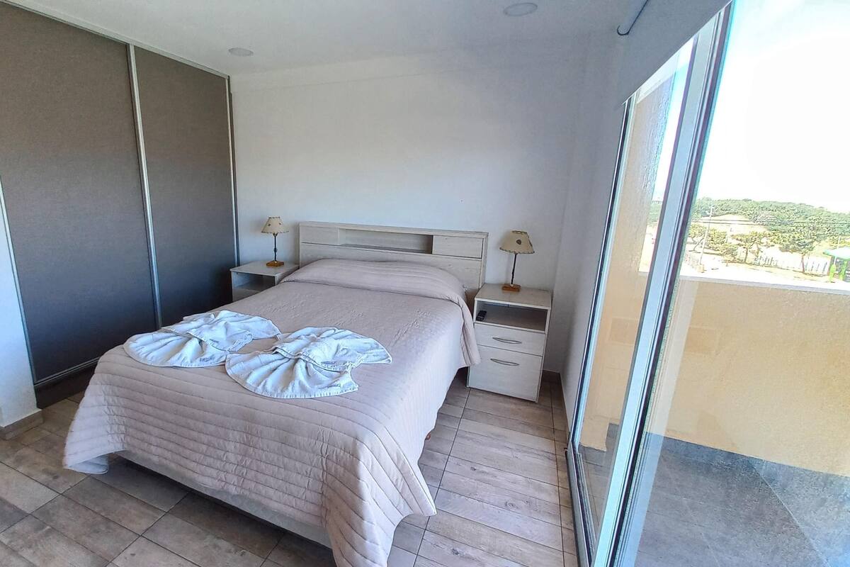 A hotel room with a bed, two bedside tables, a nightstand, a sliding door, and a view of the outdoors.