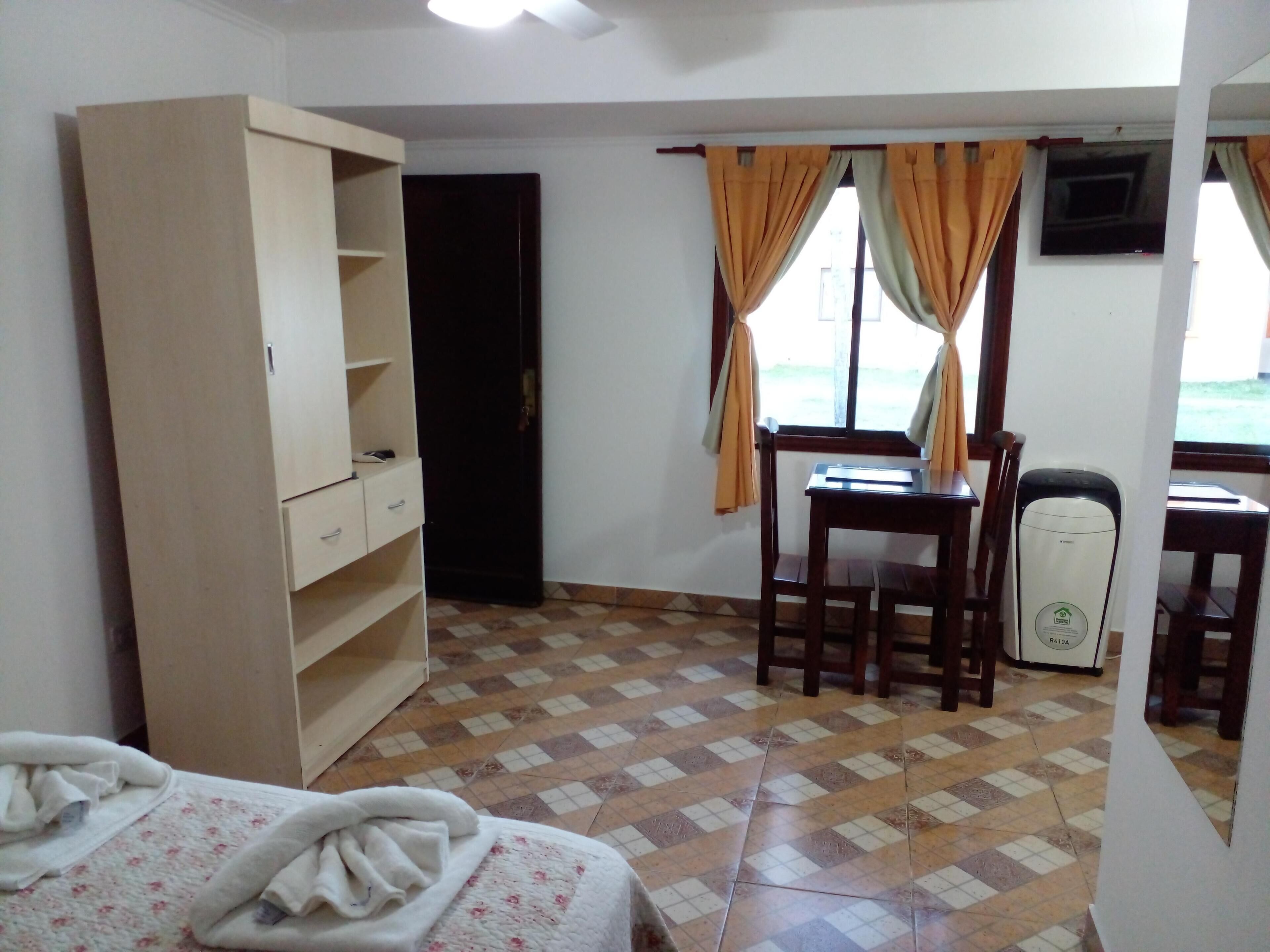 Una habitació amb llit, un armari de fusta, escriptori amb cadira, un calefactor i finestra amb cortines.