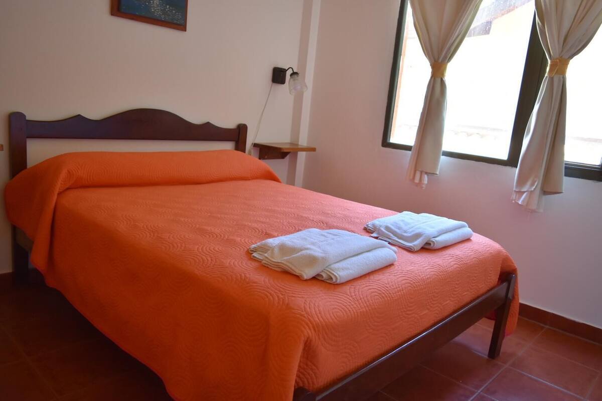 A neatly made bed with an orange bedspread and two folded white towels on the footboard.