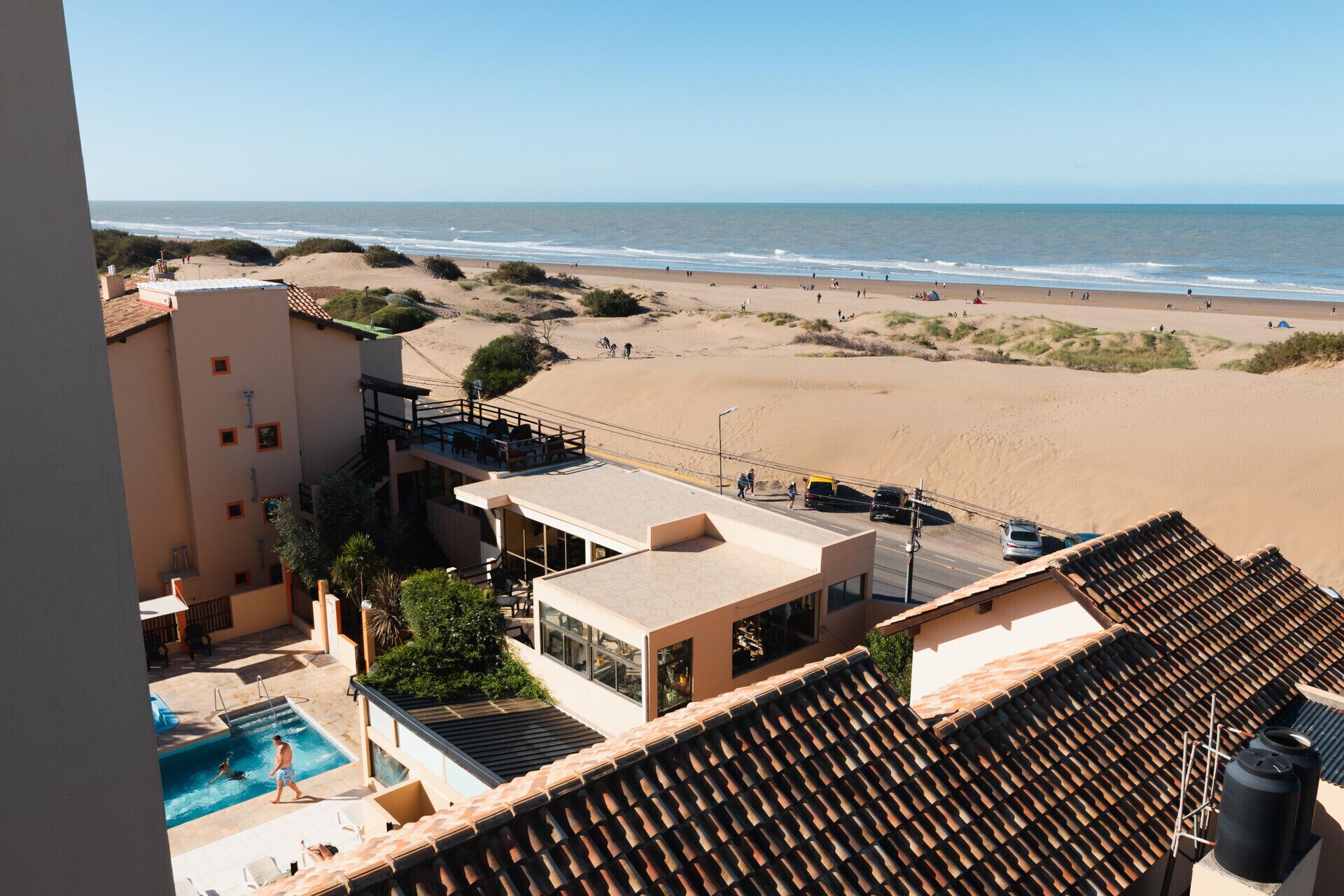 A hotel with a swimming pool, beach view, and a covered outdoor seating area.