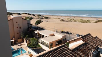 A hotel with a swimming pool, beach view, and a covered outdoor seating area.