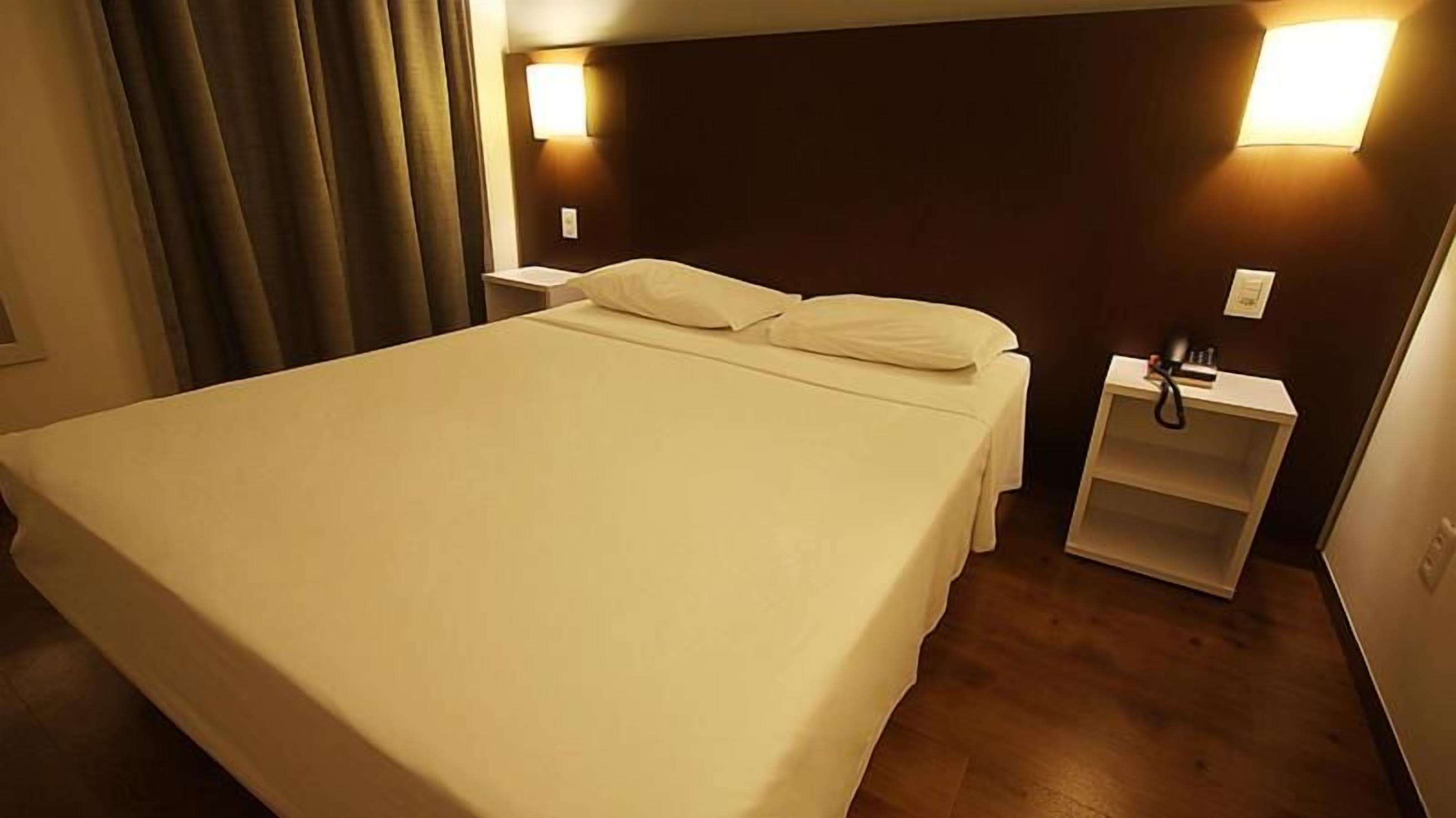 Una habitación de hotel con una cama, lámparas de noche y una mesita.