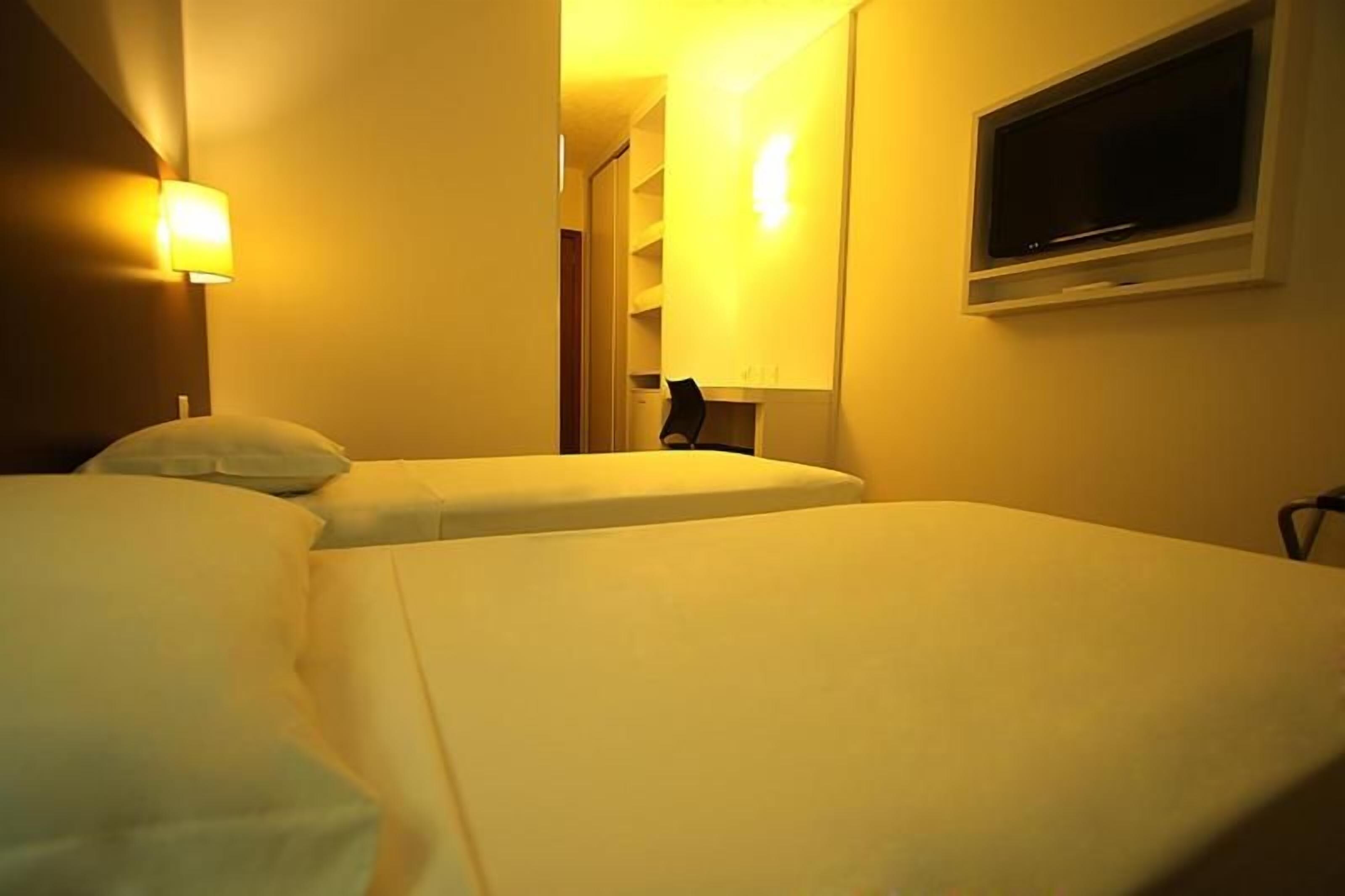 A hotel room with two beds, a television, and a wall-mounted light.