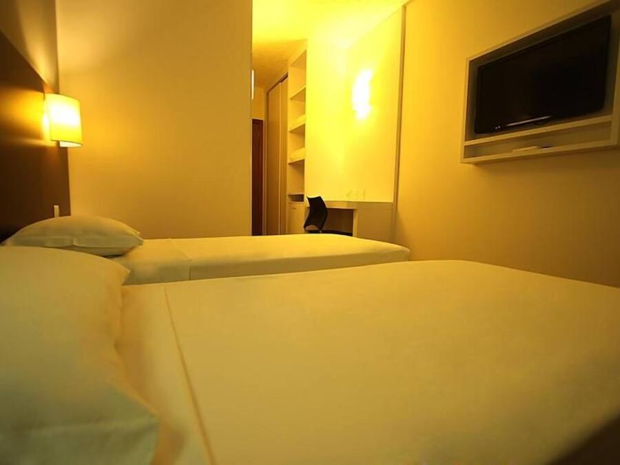 Habitació d'hotel amb dos llits, una televisió i una làmpada penjada a la paret.