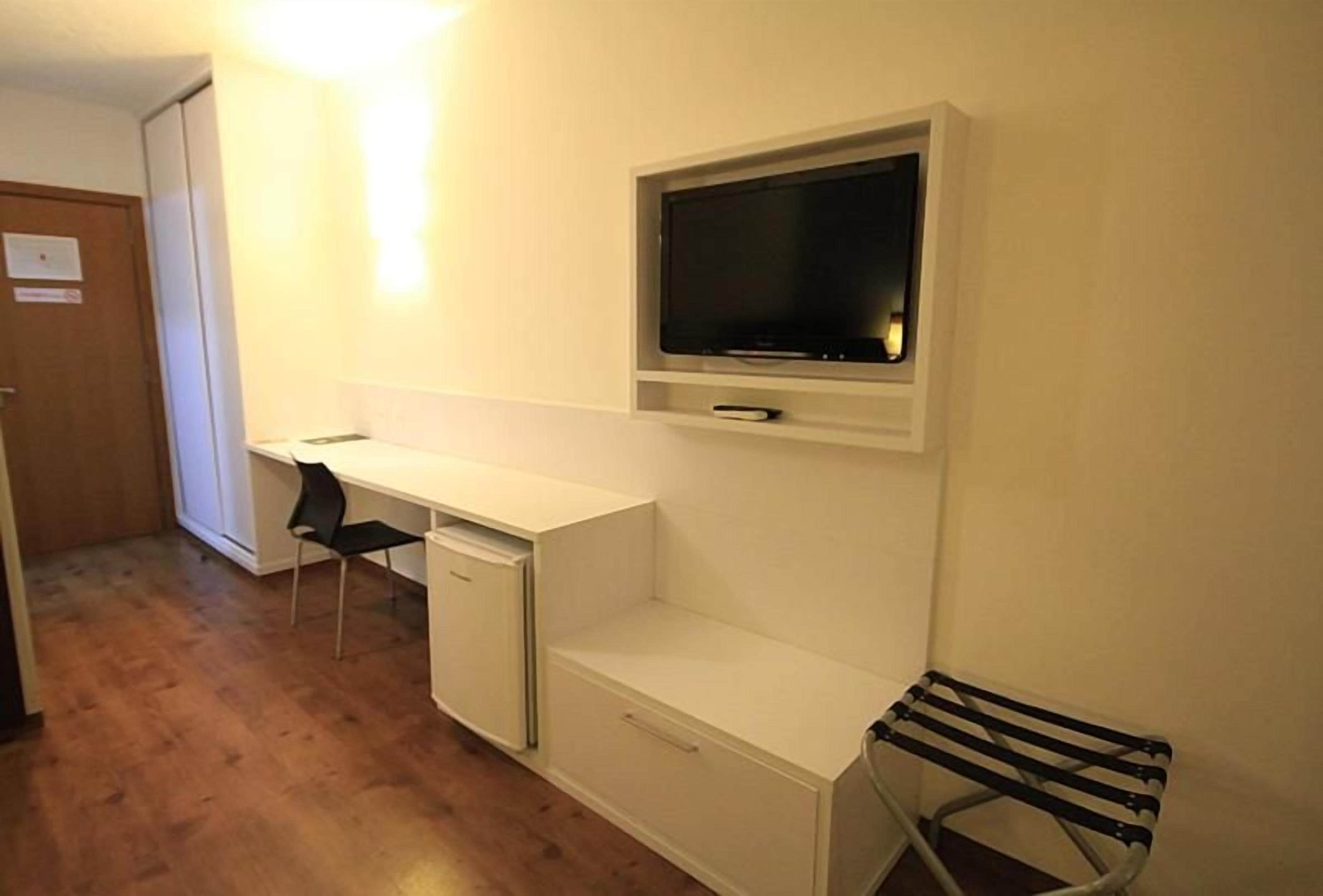 A small room with a desk, chair, and a TV mounted on the wall.