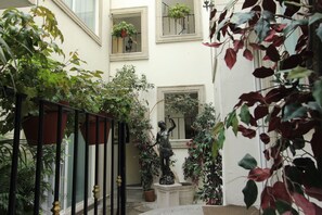 A narrow courtyard with potted plants, a statue, and a staircase. - Suites Newton (Mexico City)