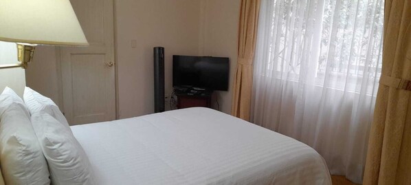 A hotel room with a bed, a television, and a window with curtains. - Suites Newton (Mexico City)
