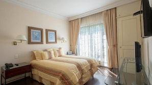 A hotel room with a bed, two framed pictures on the wall, a bedside table with a lamp, a glass table, and a TV. - Suites Newton (Mexico City)