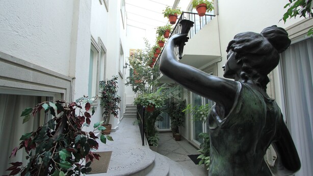 A statue in a narrow corridor with potted plants on the balconies. - Suites Newton (Mexico City)