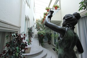 A statue in a narrow corridor with potted plants on the balconies. - Suites Newton (Mexico City)