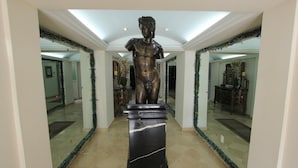 A statue on a pedestal in a hallway with mirrored walls and festive garlands. - Suites Newton (Mexico City)