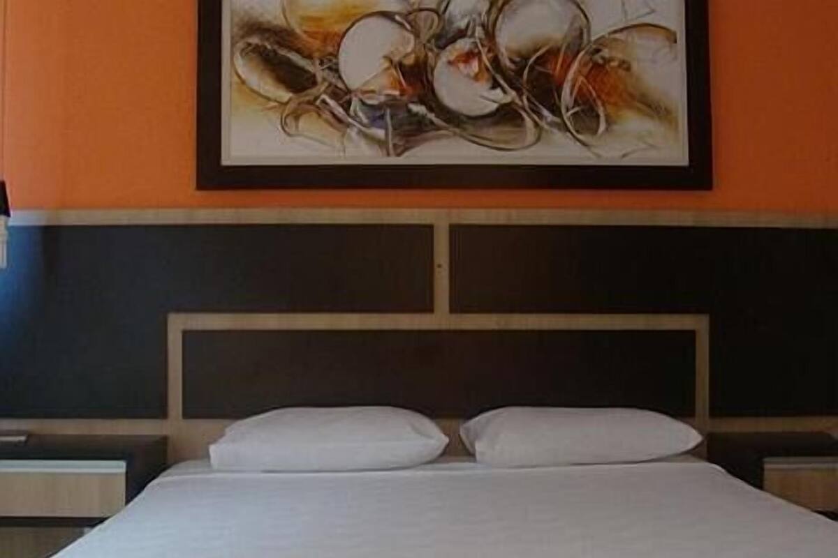 A hotel room with a bed, a headboard, and a painting on the wall.