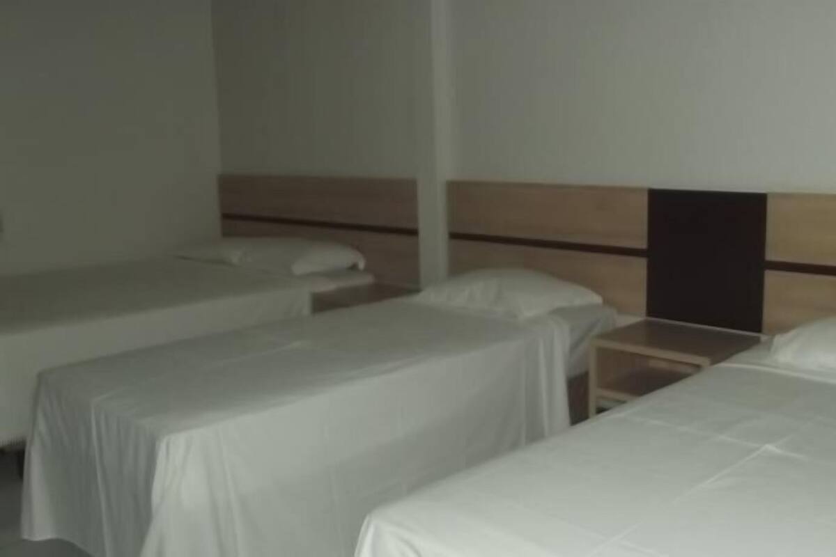 A hotel room with three single beds arranged in a row, each with a wooden headboard and white bedding.