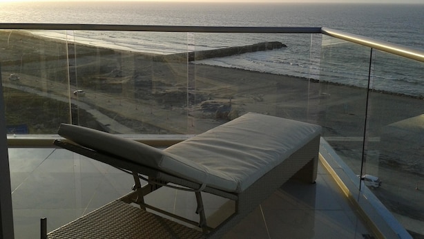 Ein Balkon mit gepolstertem Stuhl und Blick auf Strand und Meer.