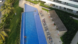 Eine Vogelperspektive zeigt ein Hotel mit einem großen Schwimmbecken, Liegestühlen und einem überdachten Sitzbereich.