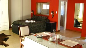Un dormitorio moderno con cama, mesitas de noche, una mesa de comedor de vidrio y un espejo grande.