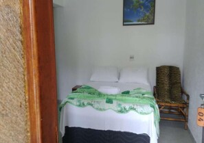 A bedroom with a bed, pillows, a green blanket, a chair, and a painting on the wall. - Hotel Alaska (Peruíbe)