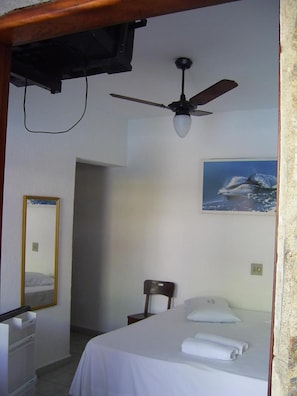 A hotel room with a bed, a ceiling fan, a painting of a whale, a mirror, and a wooden ceiling. - Hotel Alaska (Peruíbe)