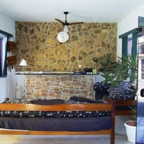 A room with a stone wall, a bed with a dark headboard, a ceiling fan, and a clock.