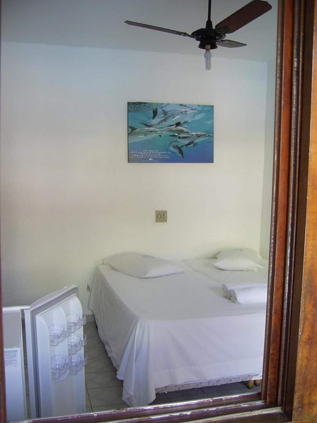 A bedroom with a bed, a ceiling fan, a wall-mounted light, and a poster.