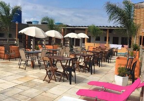 An outdoor patio area with tables and chairs, umbrellas, and potted plants. - Hotel Alaska (Peruíbe)