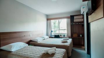A hotel room with two beds, a desk with a chair, a window with curtains, and a wardrobe.