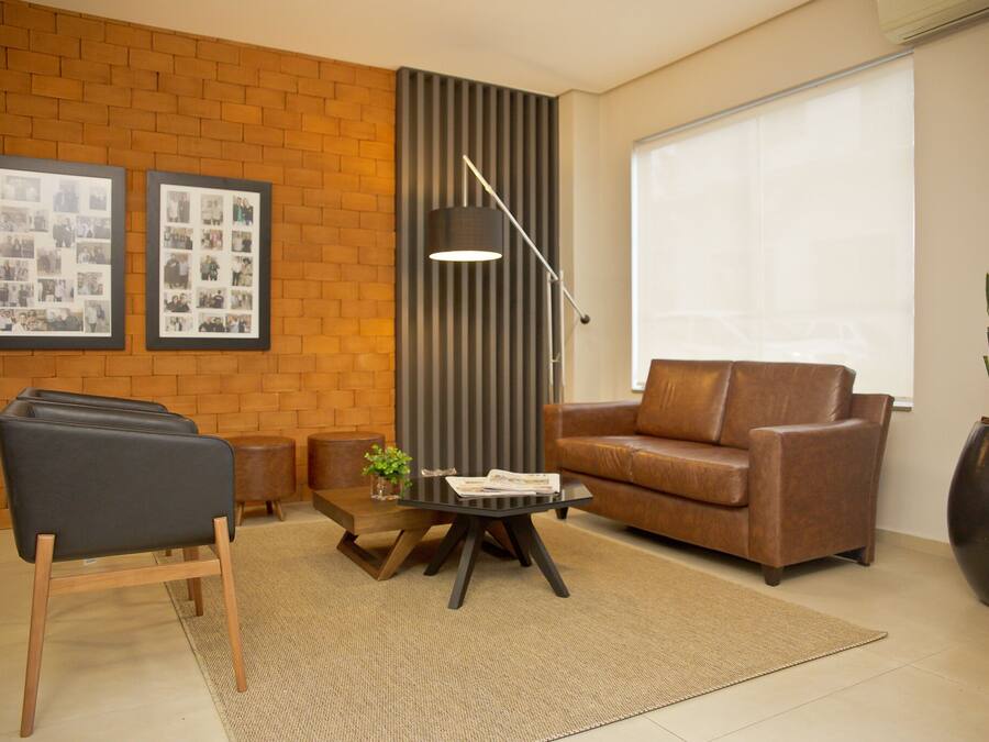 Een moderne woonkamer met een bruine leren bank, een zwarte fauteuil, een klein bijzettafeltje met tijdschriften, een vloerlamp en een grote potplant.