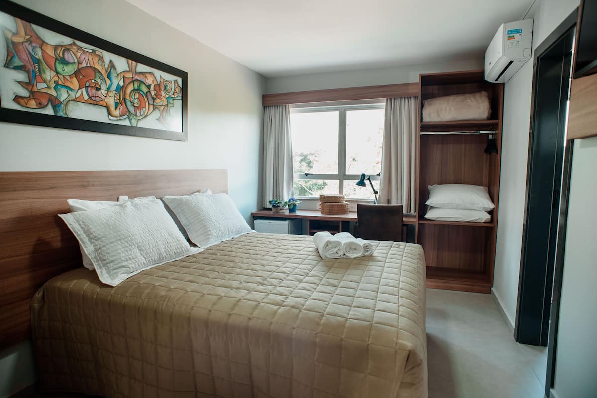 A hotel room with a bed, a desk, a chair, a window, and a wardrobe.