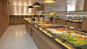 A buffet area with various food options, including salads, fruits, and beverages, in a modern setting with wooden accents and pendant lighting. - Vallér Montanha Hotel (Lajeado)