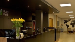 A hotel reception desk with a black counter, a wooden accent, and a vase with yellow flowers. - Vallér Montanha Hotel (Lajeado)