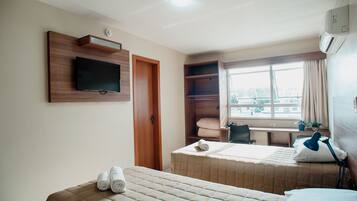 Habitación de hotel con dos camas, un televisor montado en la pared, un escritorio con una silla y una ventana con cortinas.