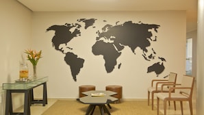 A room with a glass table, two wooden stools, a world map on the wall, and a vase with flowers. - Vallér Montanha Hotel (Lajeado)