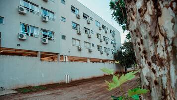 Un edificio de varios pisos con unidades de aire acondicionado en cada planta, suelo de tierra y un árbol en primer plano.
