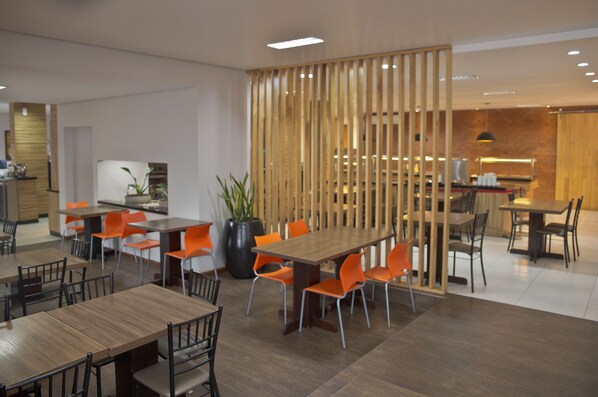 A modern dining area with wooden tables and orange chairs, a large potted plant, and a wooden partition.